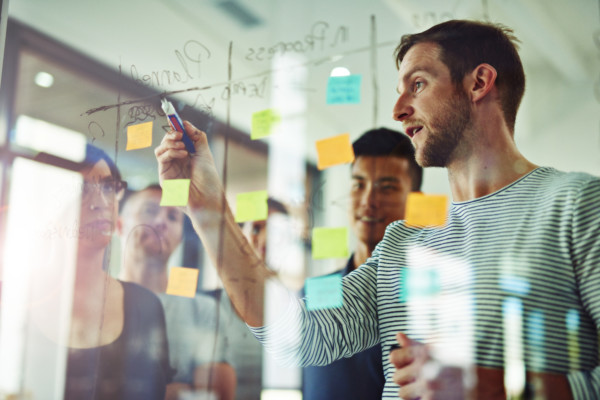 Cropped shot of coworkers using sticky notes on a glass wall during a meeting